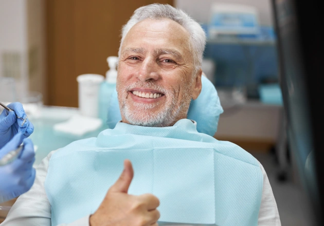 Smiling senior man giving thumbs up in dental bib at dentistry office